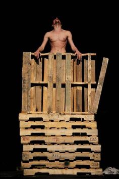 a man standing on top of a pile of wooden pallets in front of a black background