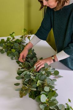 a woman arranging greenery on top of a table