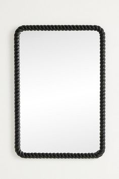 a square shaped mirror with black rope around the edges on a white wall behind it