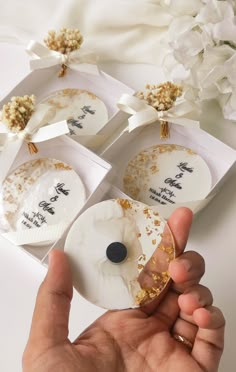 someone is holding out their wedding favors in front of the camera and flowers on the table