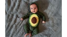 a baby in a green costume laying on a bed with an avocado cut out