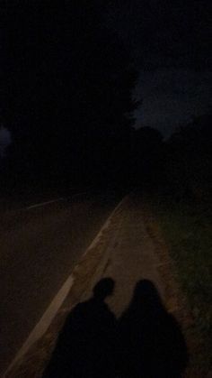 two people sitting on the side of a road at night