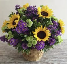 a basket filled with lots of purple and yellow flowers on top of a wooden table