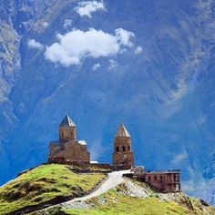 an old castle on top of a hill with mountains in the background and clouds overhead