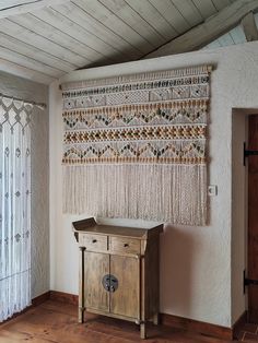 a wall hanging on the side of a white wall next to a wooden cabinet and window