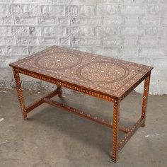 a wooden table sitting in front of a white brick wall with an intricate design on it