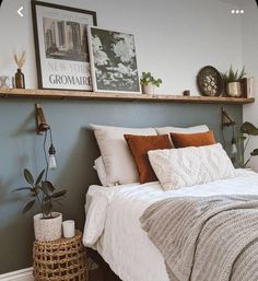 a bed with pillows and blankets on top of it next to a wooden shelf filled with potted plants