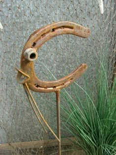 an old rusted metal object sitting on top of a wooden stand next to a green plant