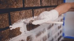 a brick wall being painted with white paint and a person holding a brush in their hand