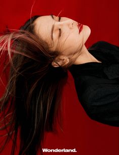 a woman with her hair blowing in the wind, wearing a black shirt and red background