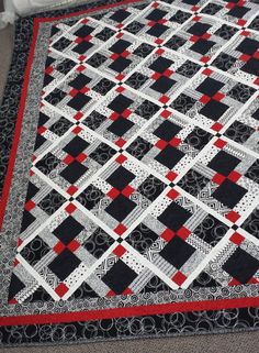 a black and white quilt with red accents on the edges, sitting on a carpet