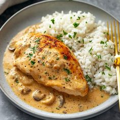 a white plate topped with rice and chicken covered in mushroom gravy next to a fork