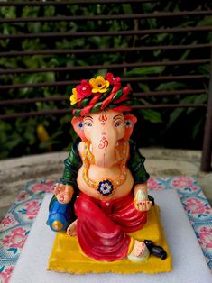 there is a small statue of an elephant sitting on a yellow platform with flowers in its hair