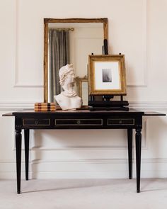 a table with a mirror and a busturine on it in front of a white wall