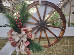 a wagon wheel decorated with pine and burlock is hung on a fence post