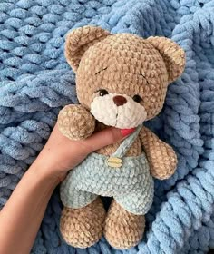 a hand holding a teddy bear on top of a blue knitted blanket with a person's finger