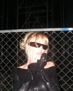 a woman wearing black gloves talking on a cell phone in front of a chain link fence