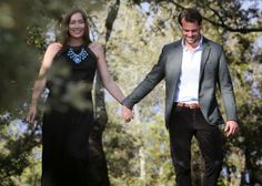 a man and woman holding hands walking through the woods