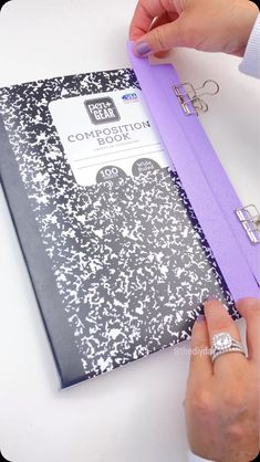 a person is holding a purple binder over a black and white book with flowers on it