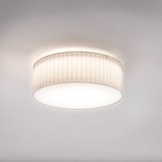 a round light fixture in a white room with dim lighting on the ceiling and wall behind it