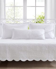 a bed with white linens and pillows in front of a window, next to a potted plant