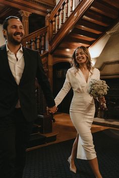 a bride and groom holding hands walking down the stairs at their wedding reception in an old building