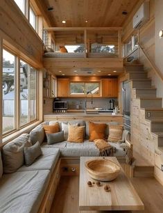 a living room filled with furniture and lots of windows next to a stair case in front of a kitchen