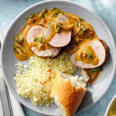 a white plate topped with meat covered in gravy next to rice and bread