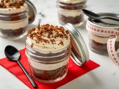 three jars filled with dessert sitting on top of a red napkin next to spoons