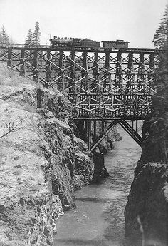 an old photo of a train crossing a bridge over a river with snow on the ground