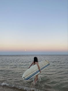 a woman carrying a surfboard into the ocean