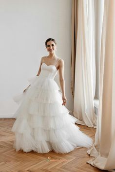 a woman in a white wedding dress standing by a window