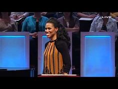 a woman standing on top of a stage in front of blue lights and people sitting behind her