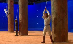 two men are performing aerial acrobatic tricks in front of blue walls and wooden pillars