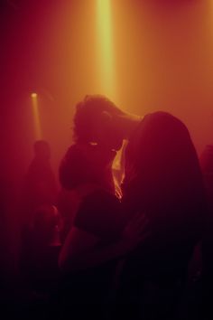 two people are standing in front of some bright lights at a concert or club with their backs to each other