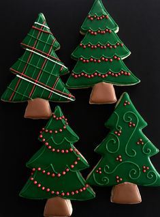 four decorated cookies in the shape of christmas trees on a black surface with red and green decorations