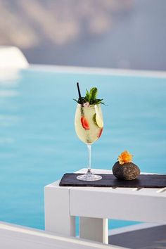 a drink sitting on top of a white table next to the ocean with fruit in it