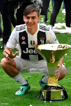 a young man kneeling on the grass with a trophy in front of him and other people behind him