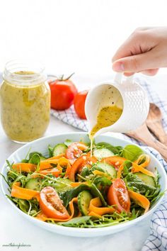 a person pouring dressing into a salad in a white bowl with cucumbers and tomatoes