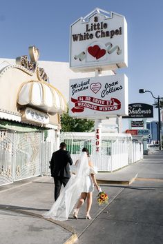 a bride and groom walking down the street in front of a little white chapel sign