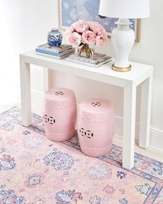 two pink stools sitting on top of a rug next to a table with flowers