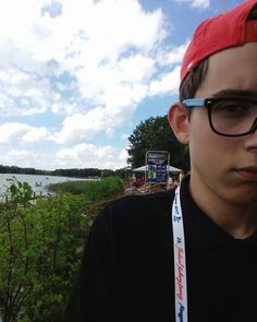 a young man wearing glasses and a red hat is looking at the camera while standing next to a lake