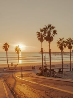 the sun is setting over the beach with palm trees and people walking on the sidewalk