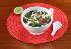 a bowl of soup with broccoli and onions on a red place mat next to a spoon