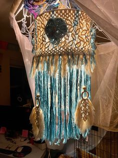 a close up of a piece of art hanging from a wire net with beads and feathers on it