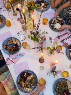 people sitting at a table with plates of food and candles in the middle of them