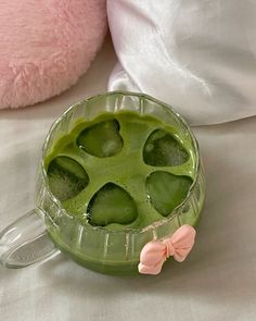 a green drink in a glass cup on a bed with a pink teddy bear next to it