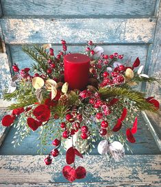 a red candle surrounded by greenery and berries on an old wooden chair with a blue background