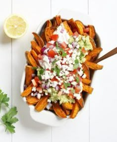 a white bowl filled with potato wedges topped with guacamole and cilantro