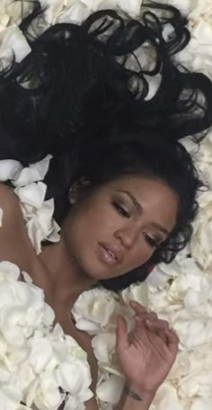 a woman laying down in white flowers with her hair flying through the air and eyes closed